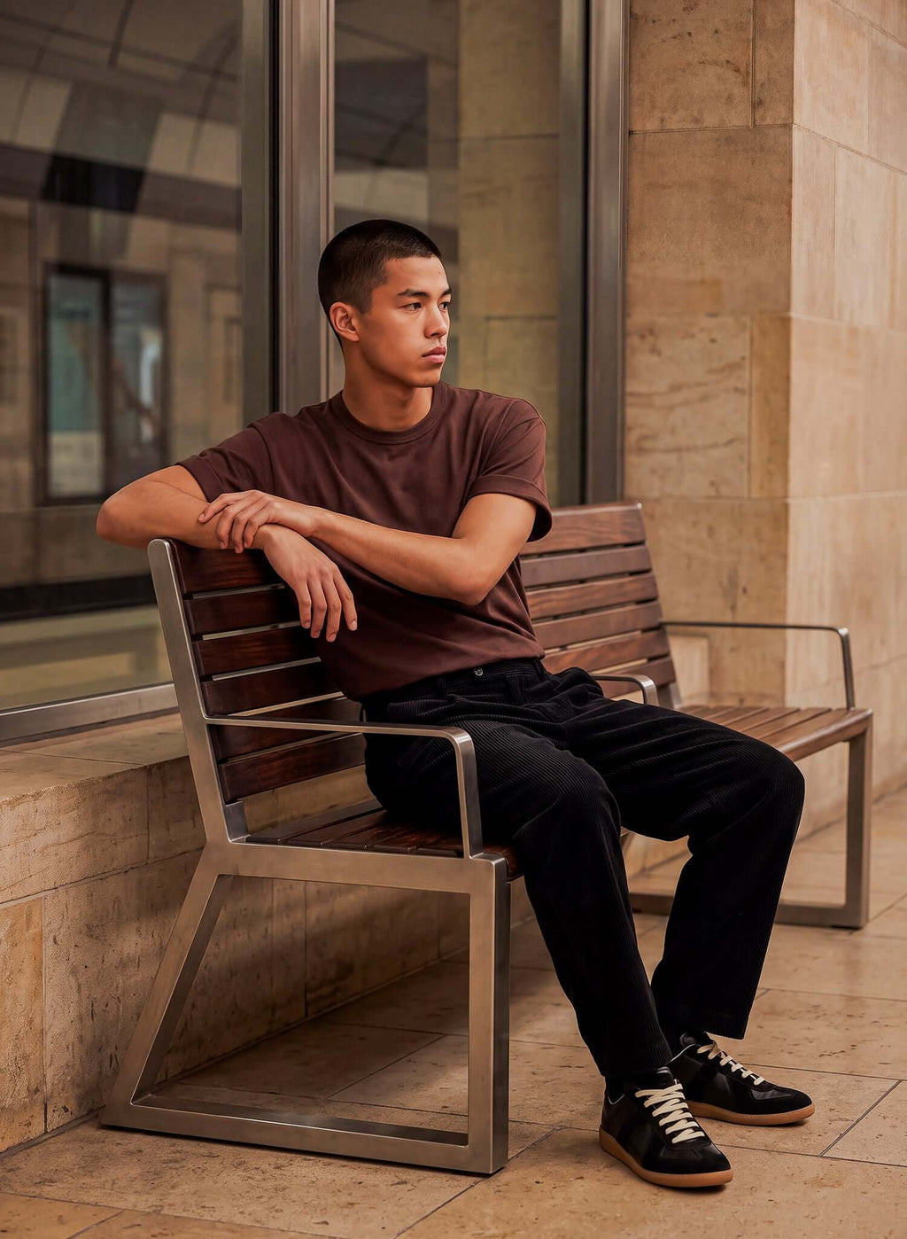 Man wearing a Men's Chocolate Brown Cotton T-shirt sitting on a bench in a modern indoor setting.