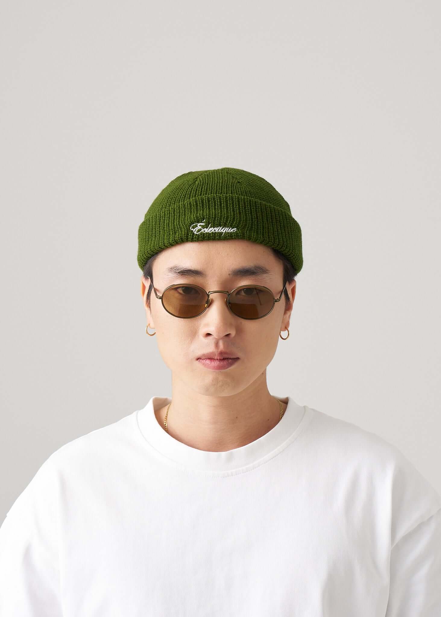Model wearing a green fisherman beanie with white logo embroidery and sunglasses, showcasing urban style.