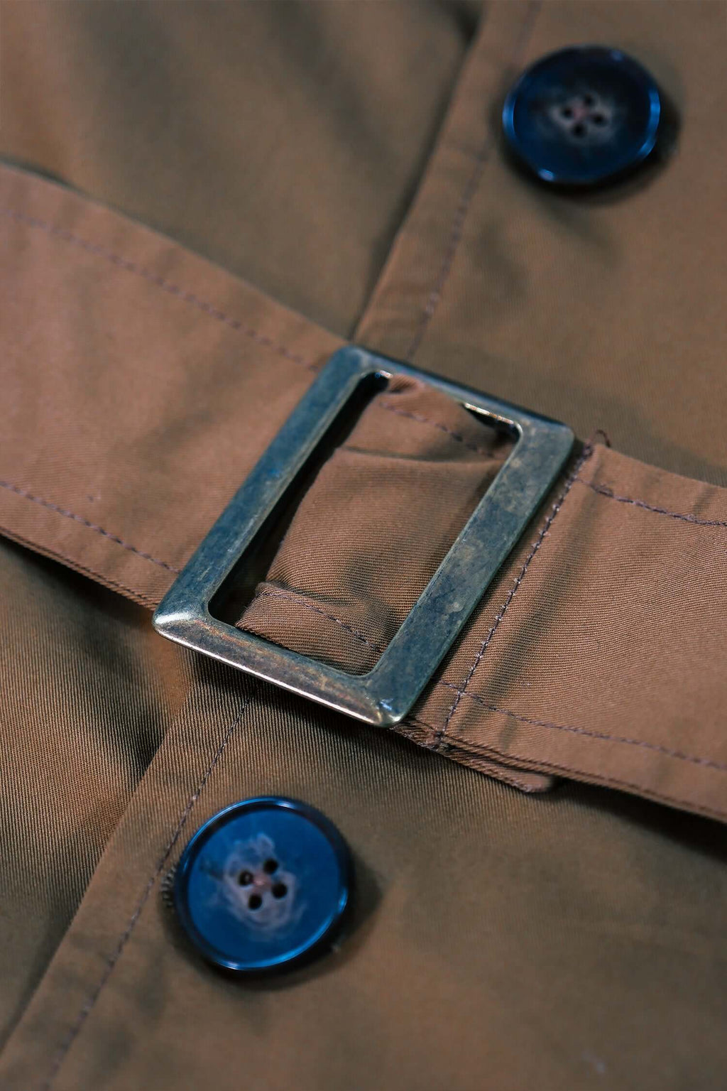 Close-up of the buckle and buttons on a men's camel trench coat, showcasing its stylish design and detail.