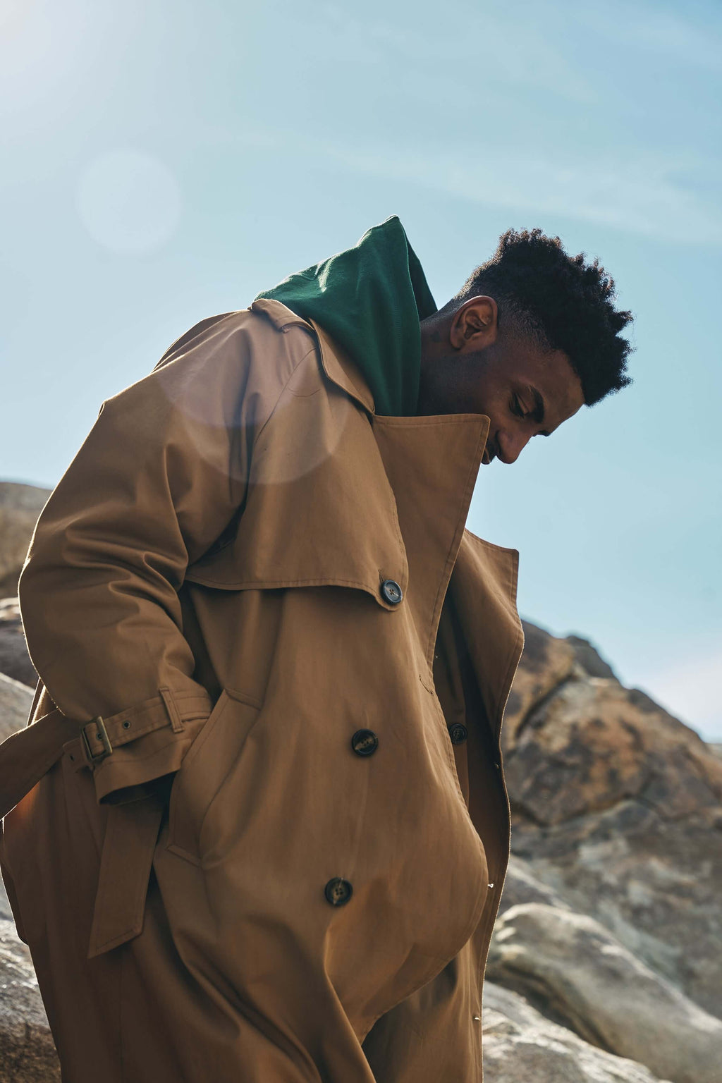 Men's camel trench coat on a model outdoors, showcasing its relaxed fit and clean design against a scenic backdrop.
