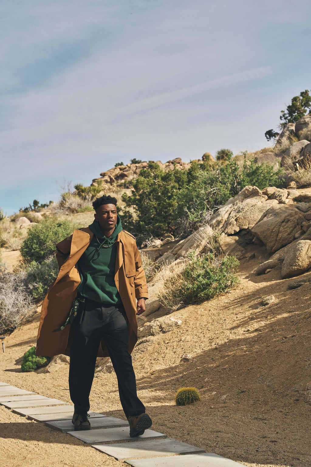 Man wearing a men's camel trench coat on a desert path, showcasing relaxed style and versatility in outdoor settings.