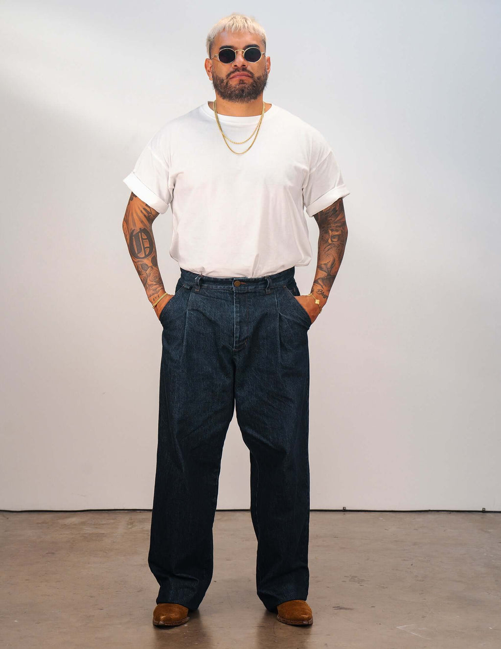 Man wearing men's indigo pleated jeans and a white t-shirt, posing confidently in a studio setting.