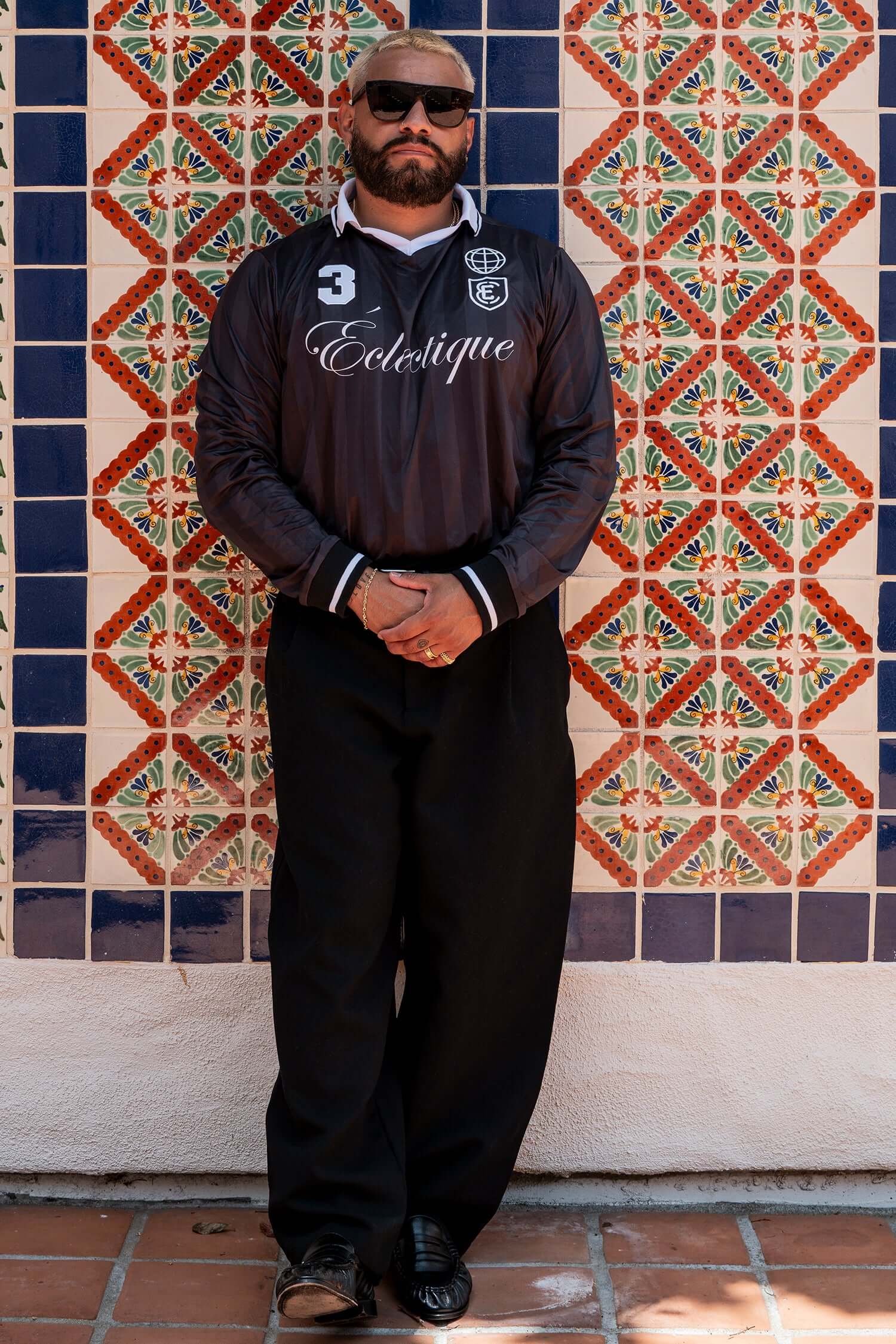 Stylish man in Long Sleeve Soccer Jersey posing against colorful tiled wall.
