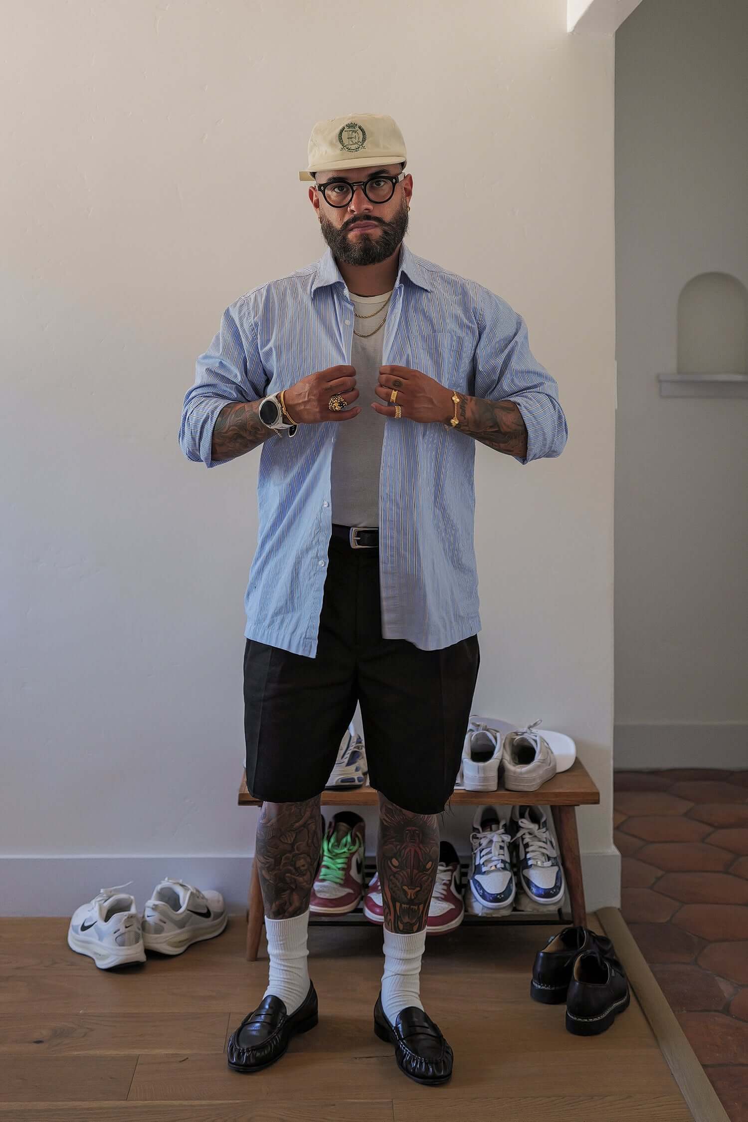 Man wearing a men's striped casual shirt in lightweight cotton, styled with shorts and accessories, standing indoors.