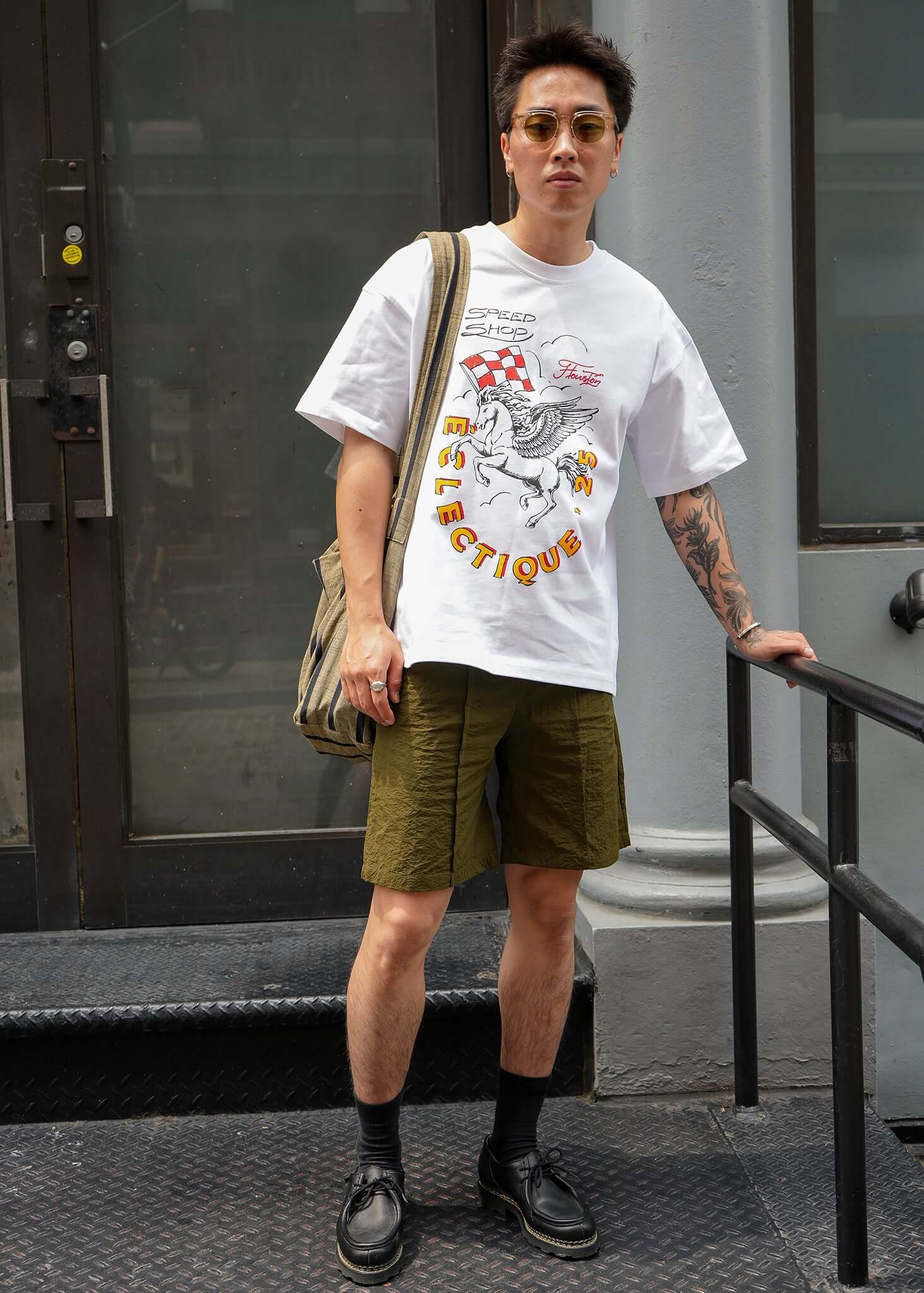 Young man wearing Racing Graphic T-shirt from Éclectique Speed Shop with olive shorts and sunglasses.