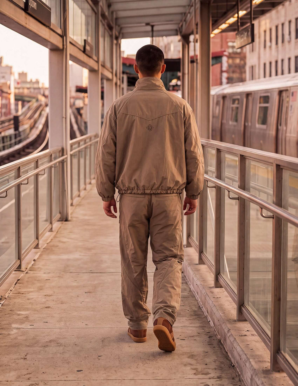 Man walking away wearing the Waypoint Lightweight Anorak in Clay on a transit platform during sunset.