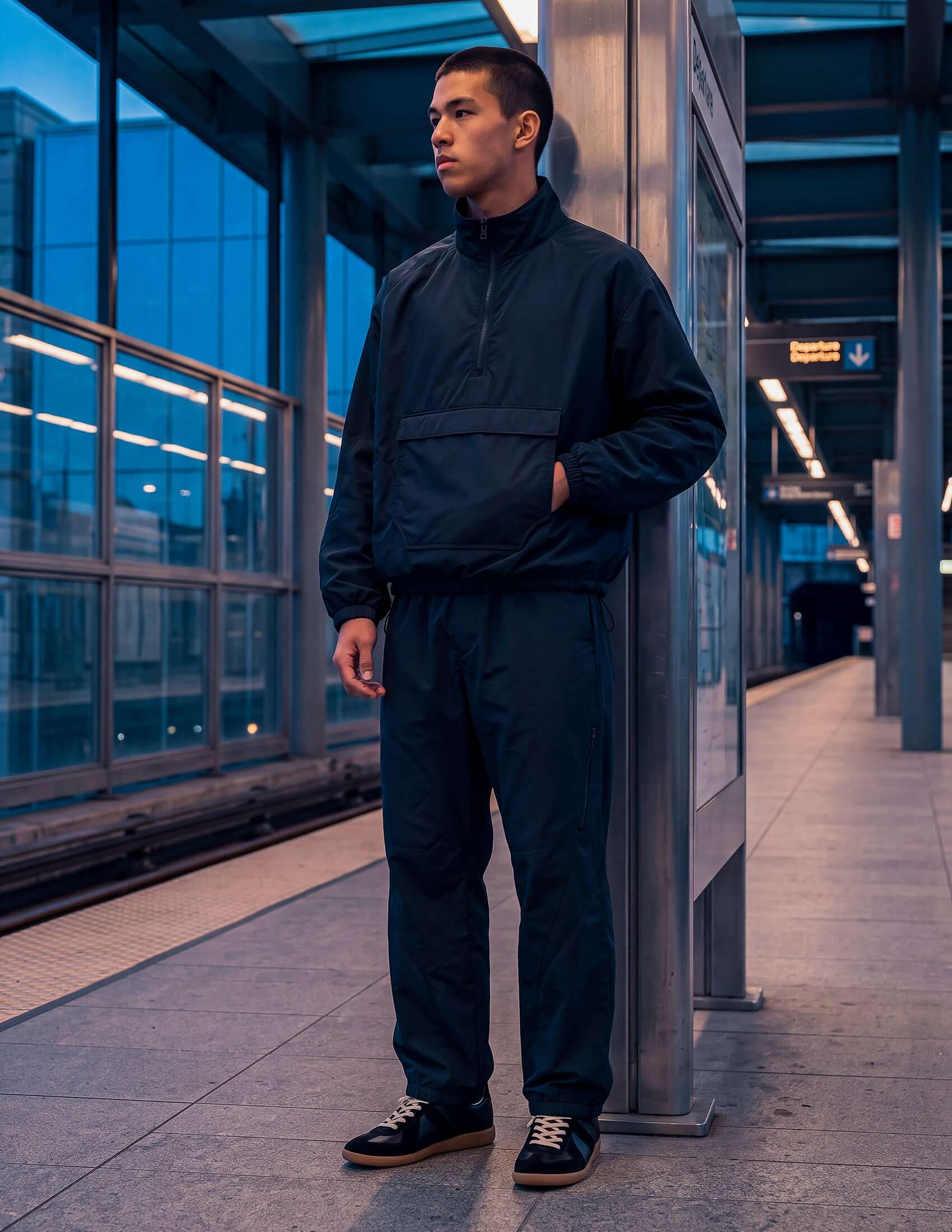 Model wearing the Waypoint Lightweight Anorak in Midnight Navy at a train station, showcasing its relaxed design and technical features.