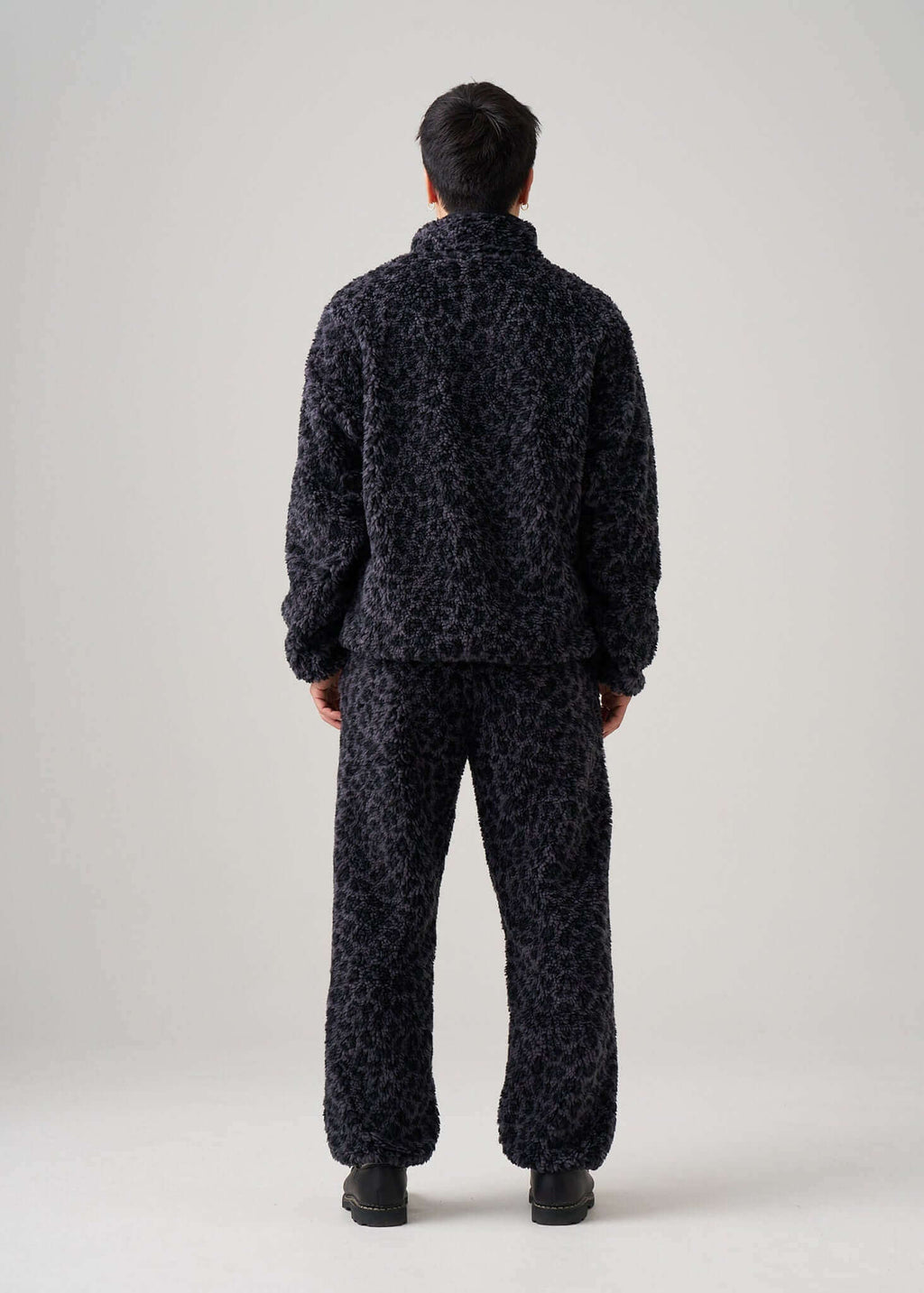 Back view of a model wearing black leopard fleece pants and a matching fleece jacket.