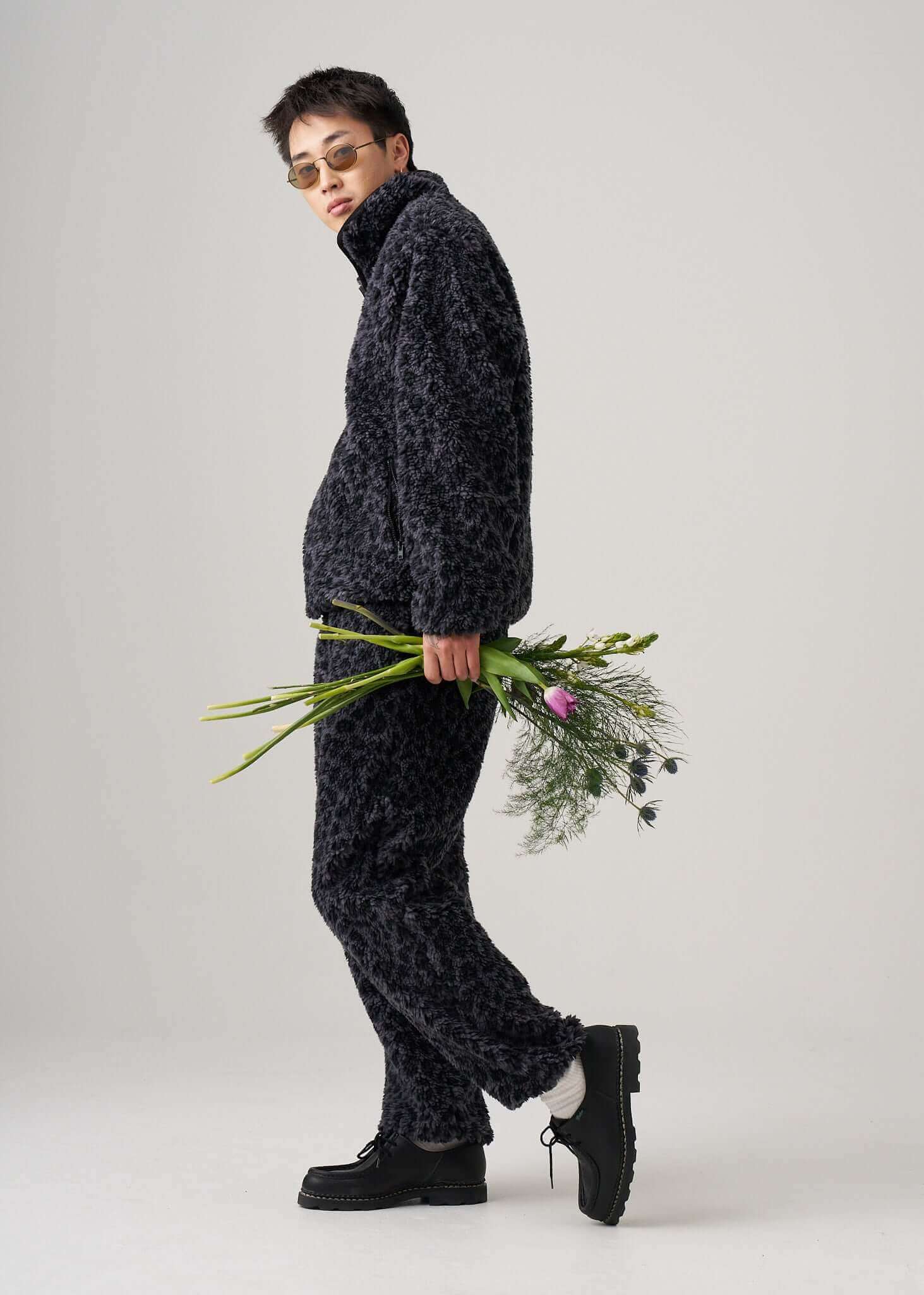 Model wearing black Leopard fleece pants with a matching jacket, holding flowers, showcasing casual style.