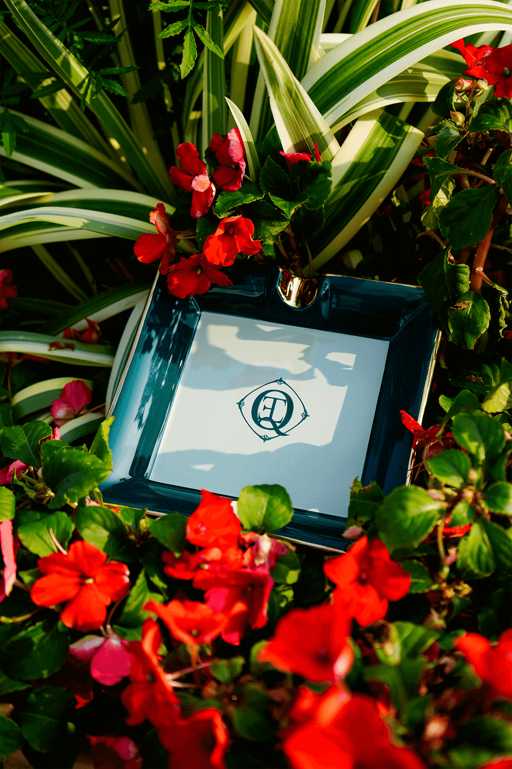 Ceramic Cigar Ashtray surrounded by vibrant red flowers in a lush garden setting.