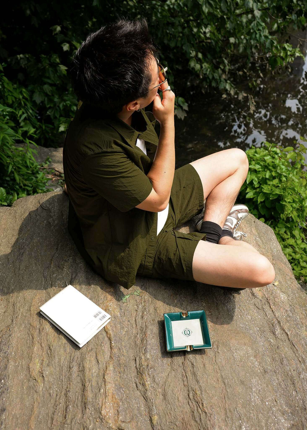 Man enjoying a moment outdoors with a Ceramic Cigar Ashtray on a rock beside a notebook.