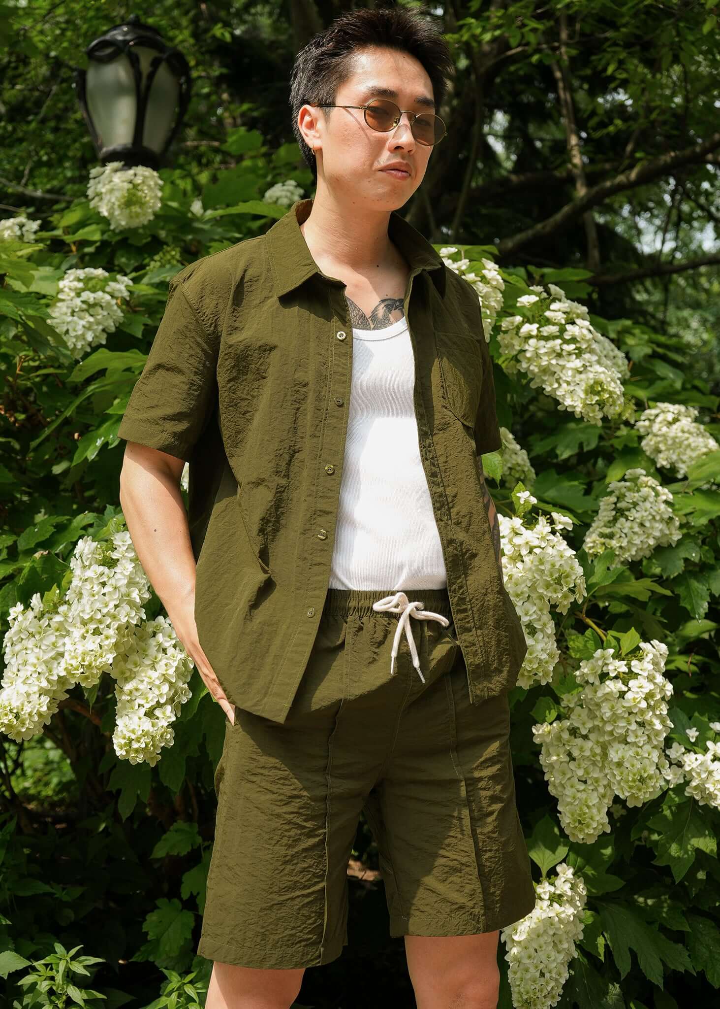Model wearing designer men's casual shorts made from 100% nylon in olive green with cream drawstring on a sunny day.