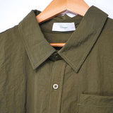 Close-up of a designer short sleeve casual shirt in olive green hanging on a wooden hanger.