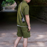 Man wearing a designer short sleeve casual shirt in olive green, styled with shorts and sneakers.