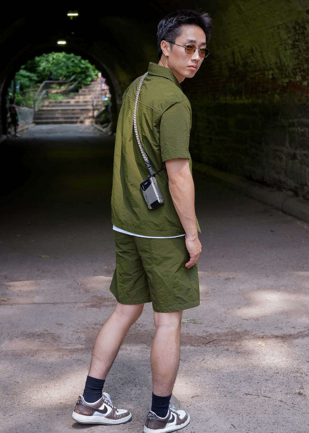 Man wearing a designer short sleeve casual shirt in olive green, styled with shorts and sneakers.