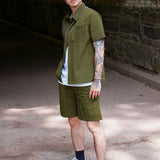 Man wearing a stylish olive designer short sleeve casual shirt paired with shorts in an outdoor setting.