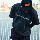 Model wearing Eclectique t-shirt and cap by the waterfront with a city skyline in the background.
