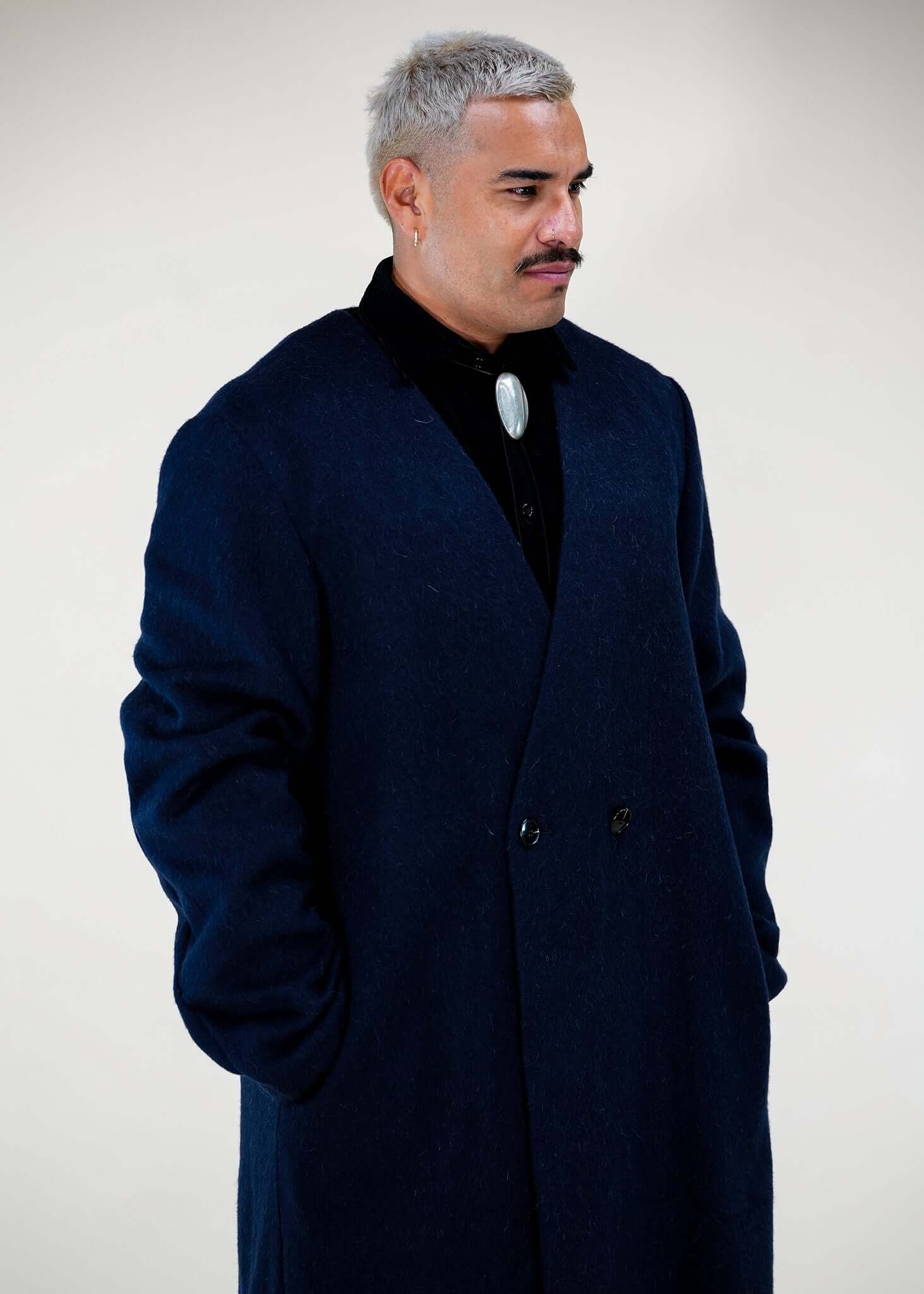Model wearing Éclectique collarless long coat in navy front three-quarter view