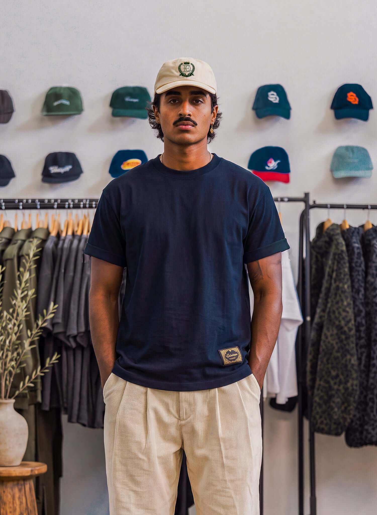 Japanese Made Essential Cotton T-shirt in navy worn by a model, featuring relaxed fit and clean crew neckline, amidst a display of caps.