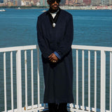 Model wearing the Kanso Collarless Long Coat with city skyline and waterfront in the background.
