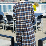 Back view of a man wearing a Kanso Plaid Collarless Long Coat, showcasing the elegant plaid pattern against a city backdrop.