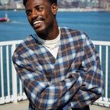 Model wearing a stylish plaid collarless long coat by Éclectique against a waterfront city backdrop.