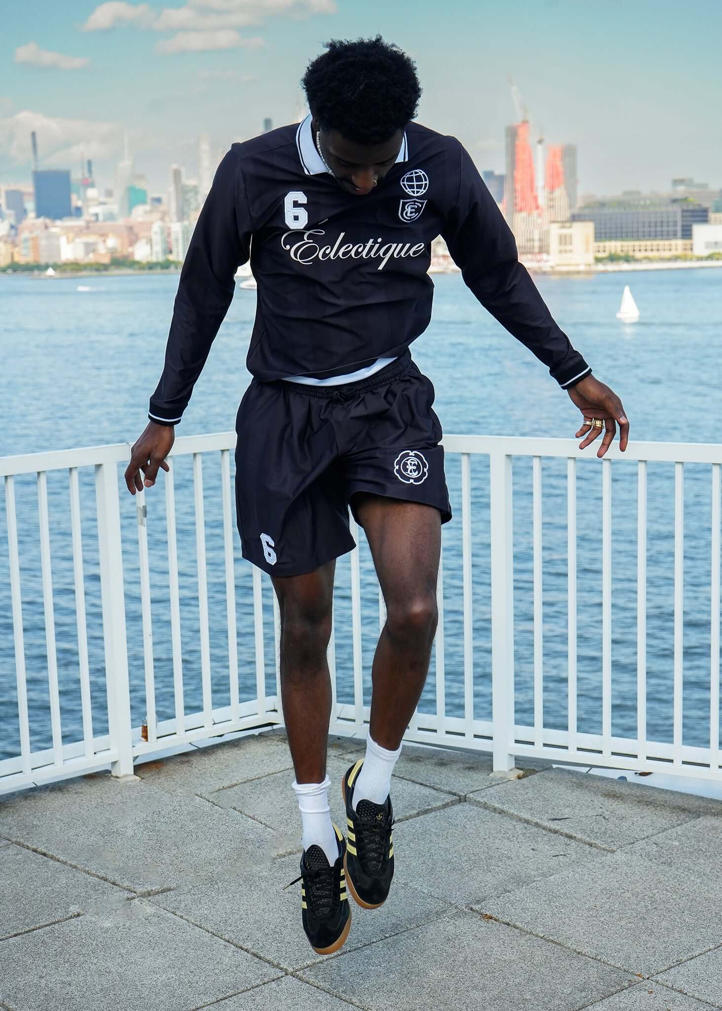 Long Sleeve Soccer Jersey featuring a player jumping, wearing black jersey and shorts by the waterfront.