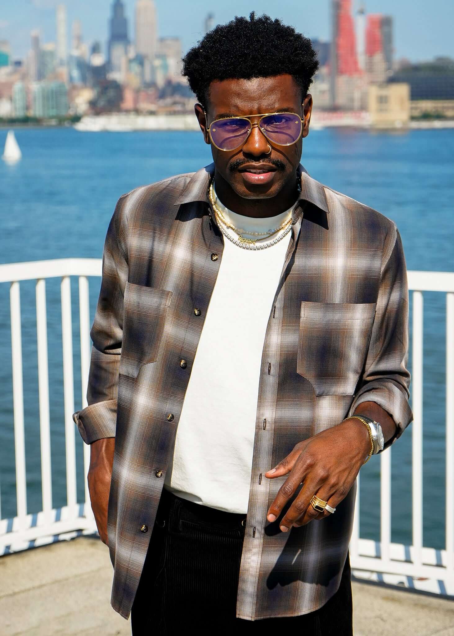 Man wearing a Mercer Plaid Cotton Button-Up Shirt with sunglasses by the water, showcasing modern menswear style.