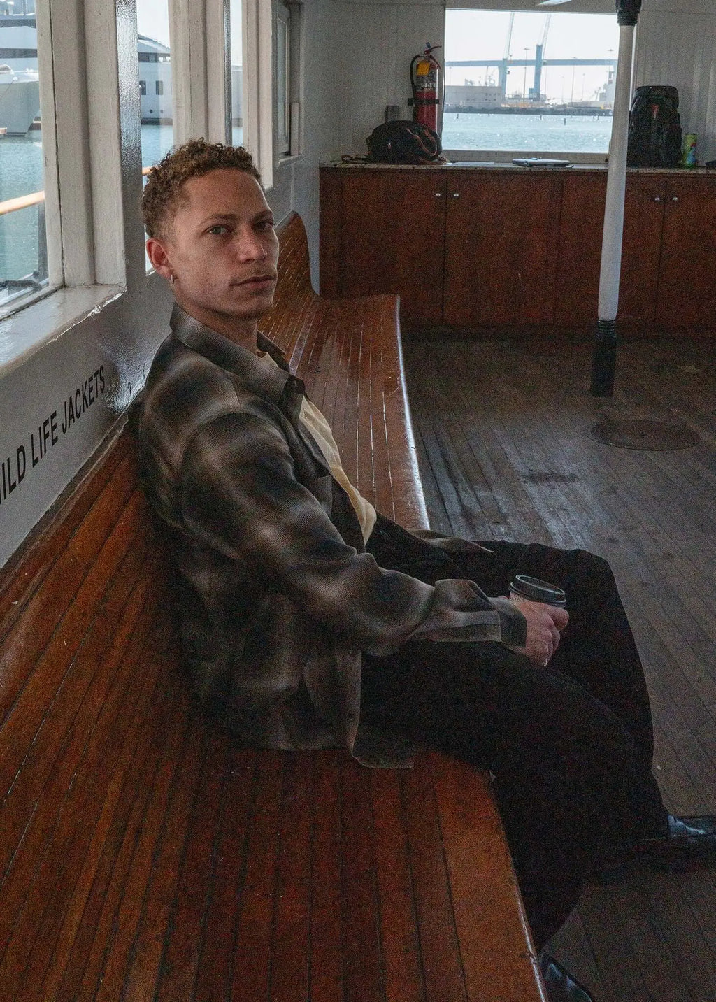 Person wearing a plaid cotton button-up shirt sitting on a wooden bench, showcasing a casual style.