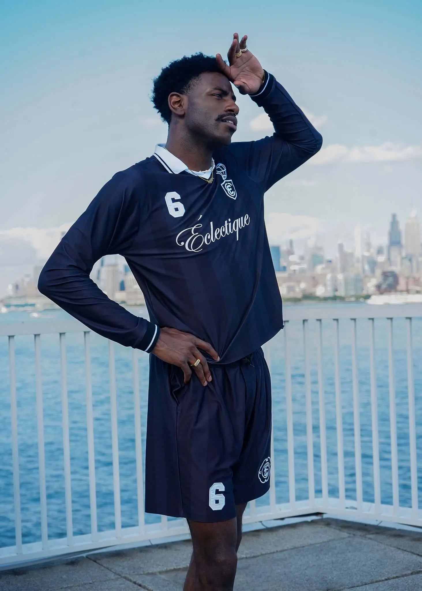 Man wearing men's black soccer shorts by Éclectique, posing outdoors with city skyline in background.