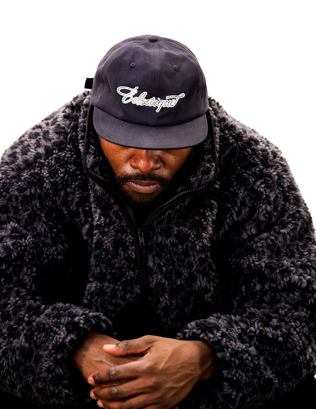 Rope script dad hat worn by a person in a black fur jacket, close-up view showcasing the embroidered design.