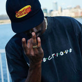 Person wearing Seinfeld Vintage logo hat, with an embroidered design, posing near a waterfront.