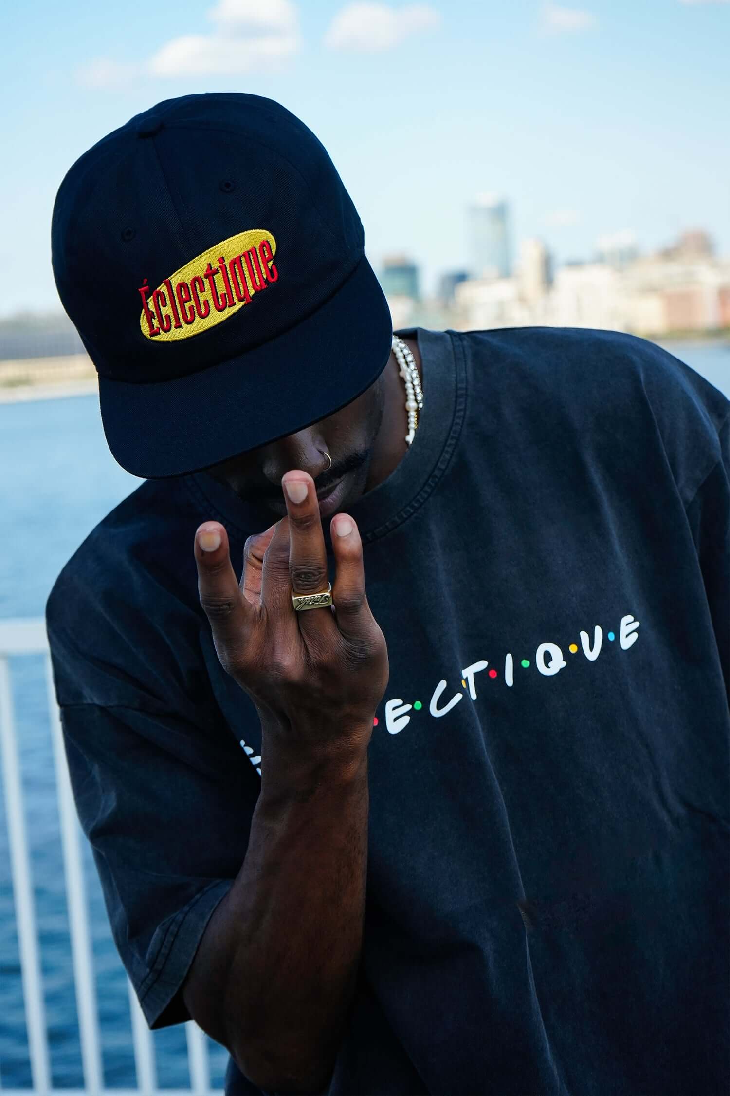 Person wearing Seinfeld Vintage logo hat, with an embroidered design, posing near a waterfront.