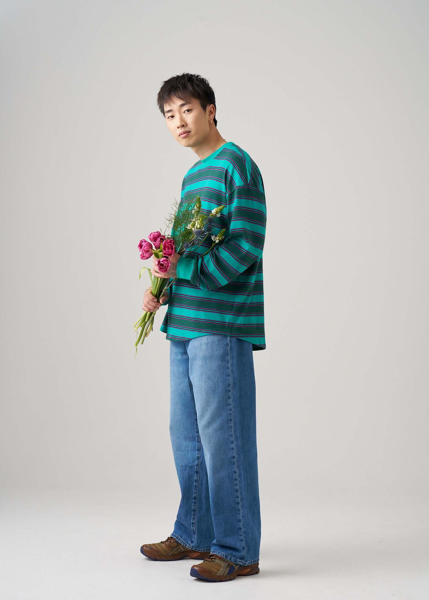Model wearing a long sleeve t-shirt in Emerald Drift with flowers, showcasing a relaxed style with blue jeans.
