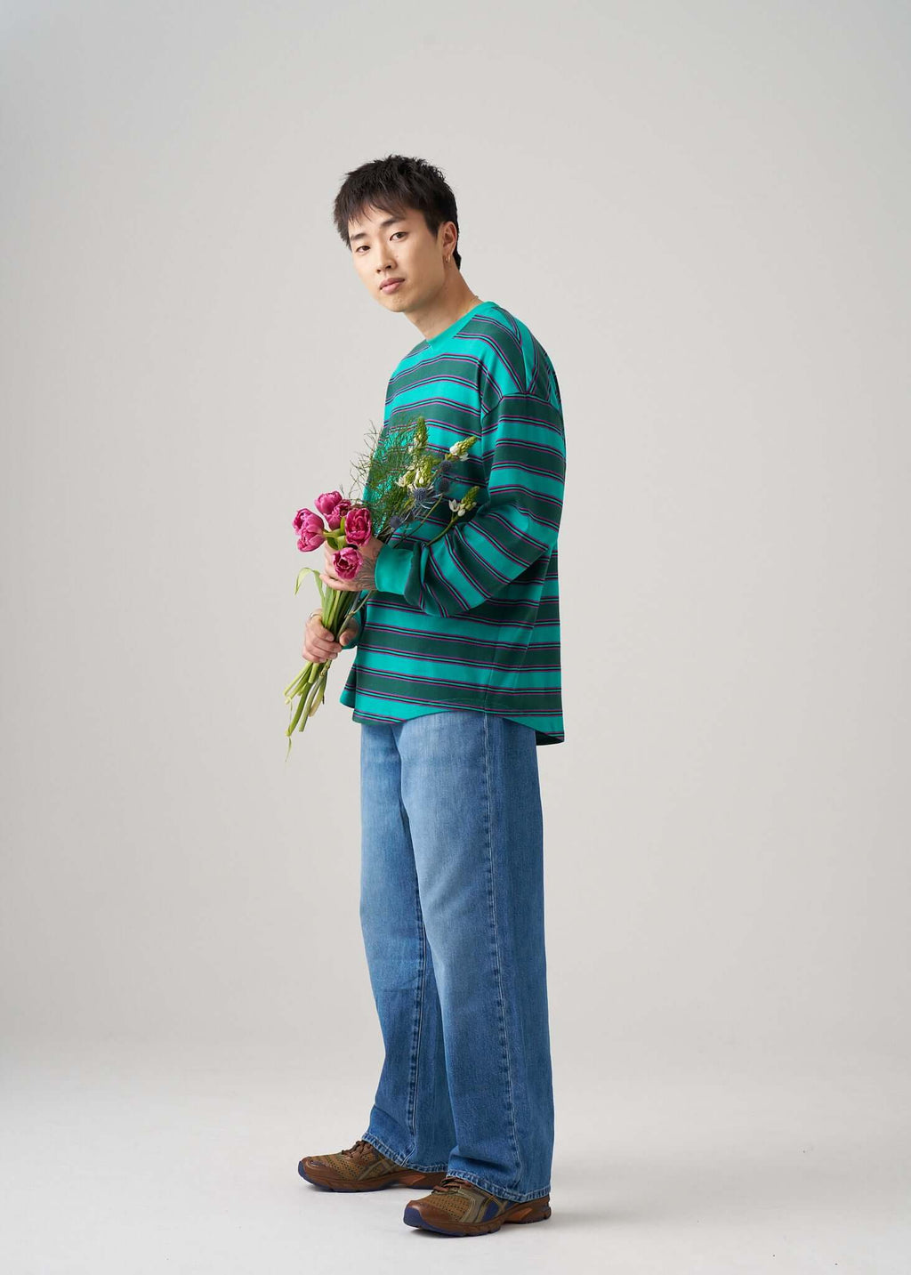 Model wearing a long sleeve t-shirt in Emerald Drift with flowers, showcasing a relaxed style with blue jeans.