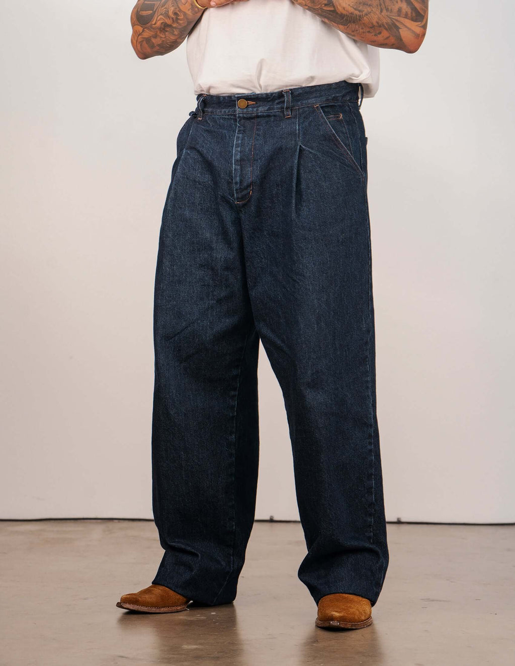 Men's indigo pleated jeans worn by a model, showcasing a relaxed wide-leg silhouette and sharp front pleats.