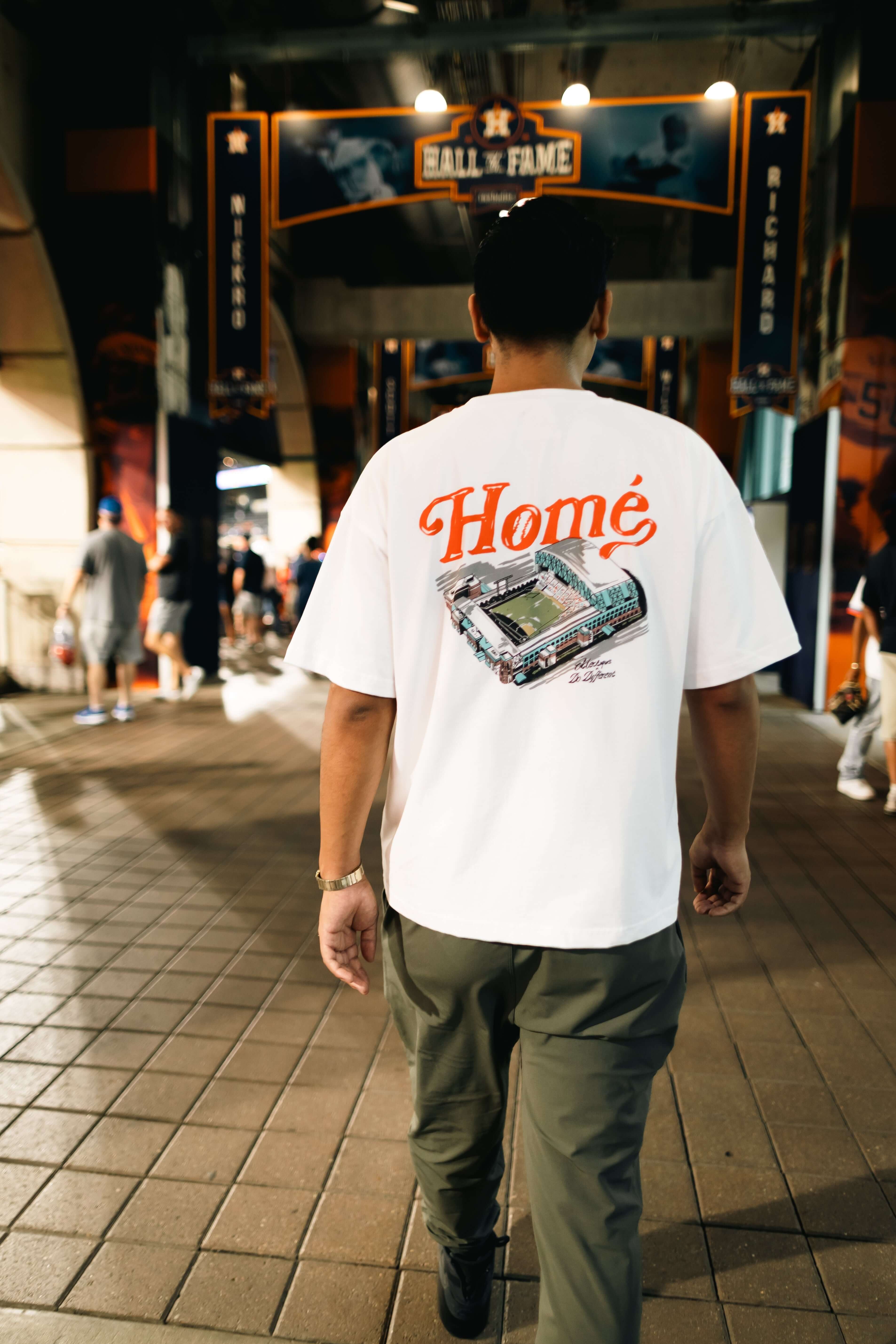 A person wearing a Home collaboration T-shirt – Éclectique x Do Different walking in a stadium setting