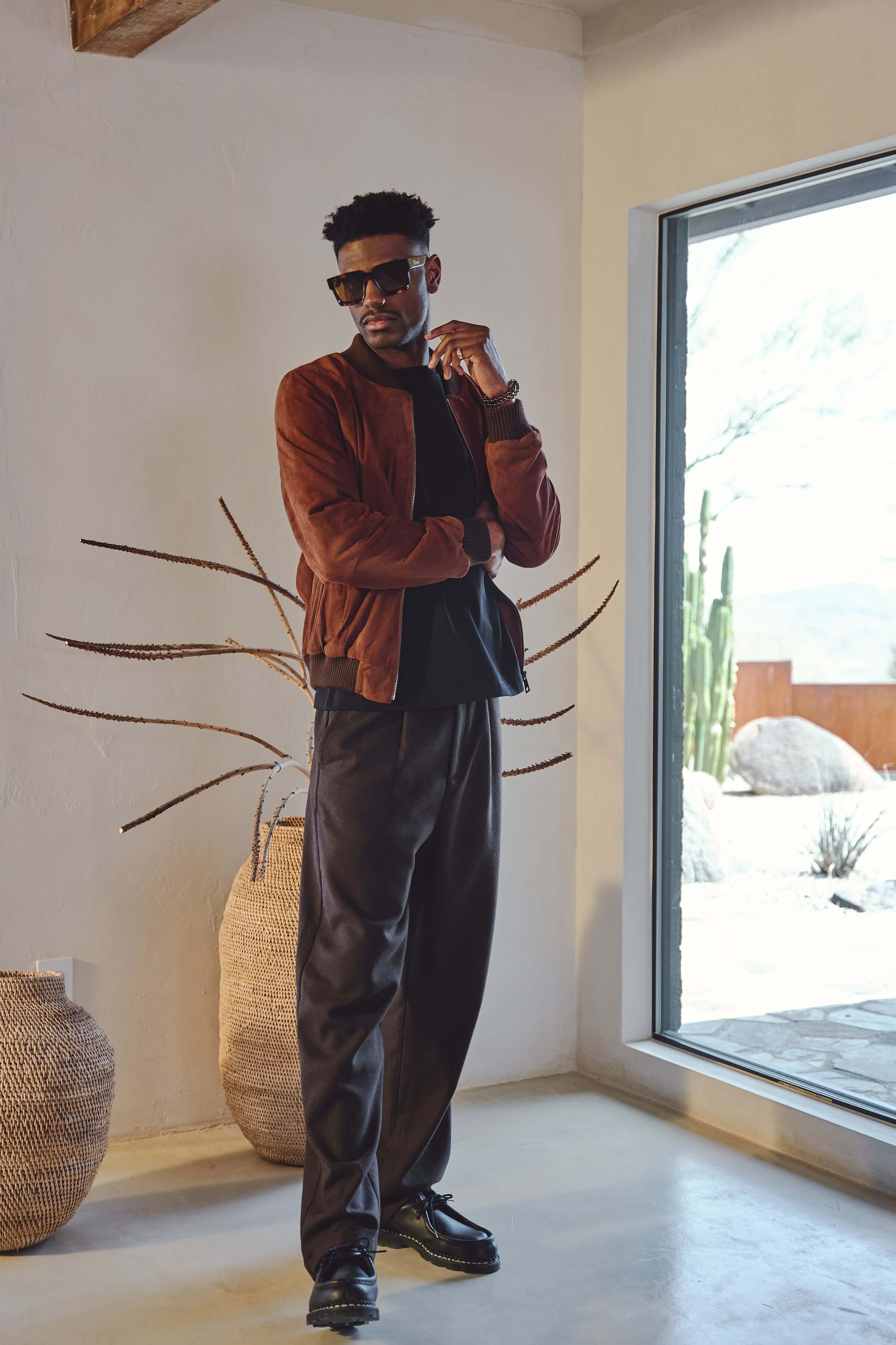Model wearing Éclectique Italian suede bomber jacket in brown styled with black trousers