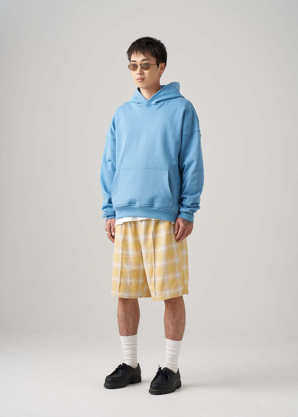 A model wearing a lightweight terry hoodie in cotton jersey with yellow plaid shorts and sunglasses.
