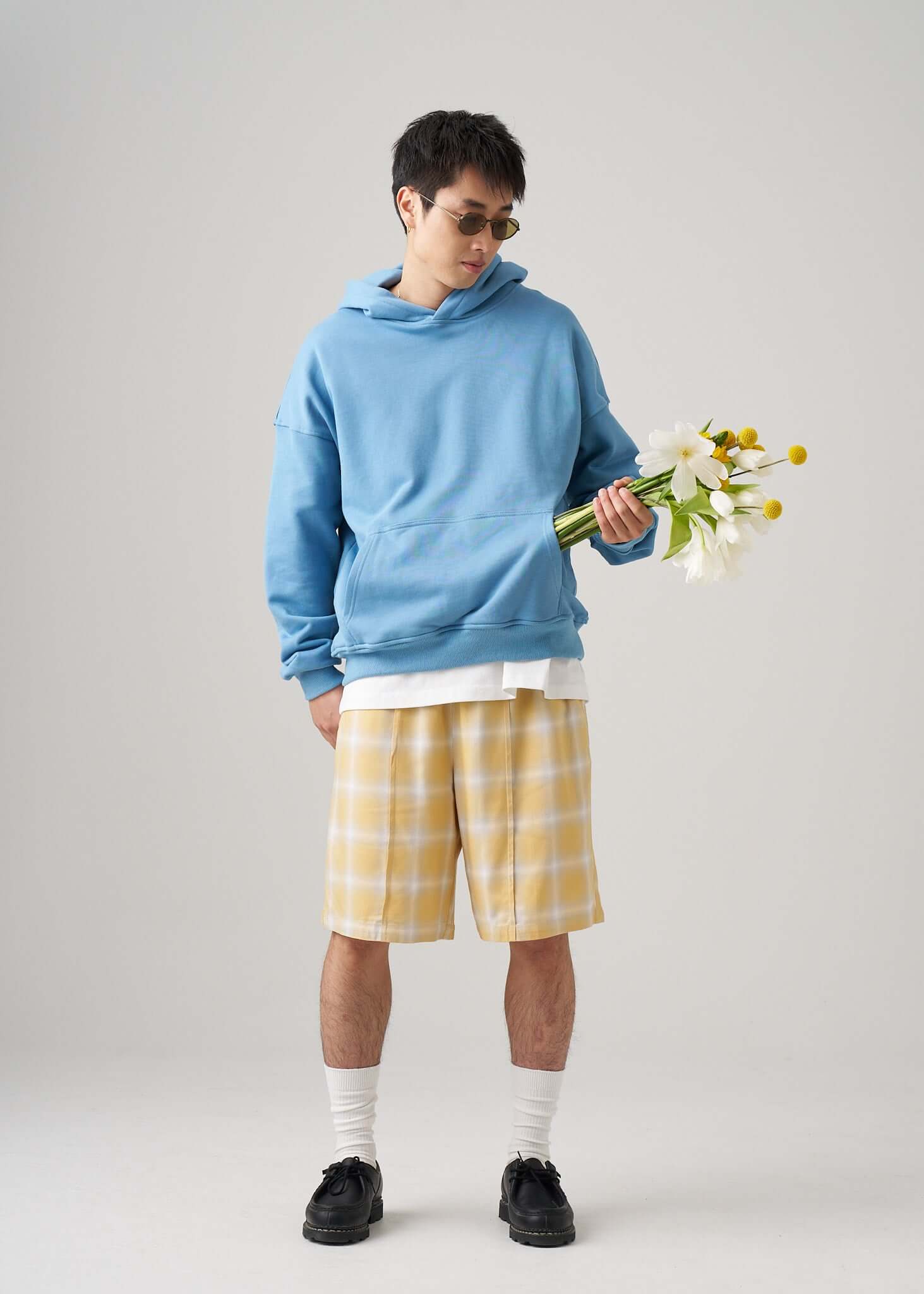 Model wearing a lightweight terry hoodie in light blue with floral bouquet, paired with yellow plaid shorts.