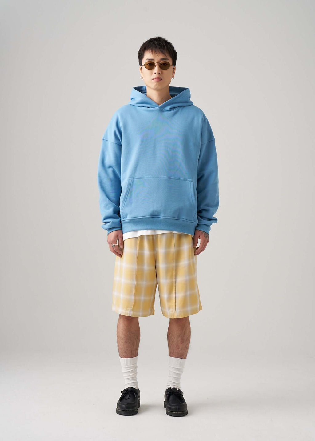 Model wearing a lightweight terry hoodie in blue with yellow plaid shorts and sunglasses.