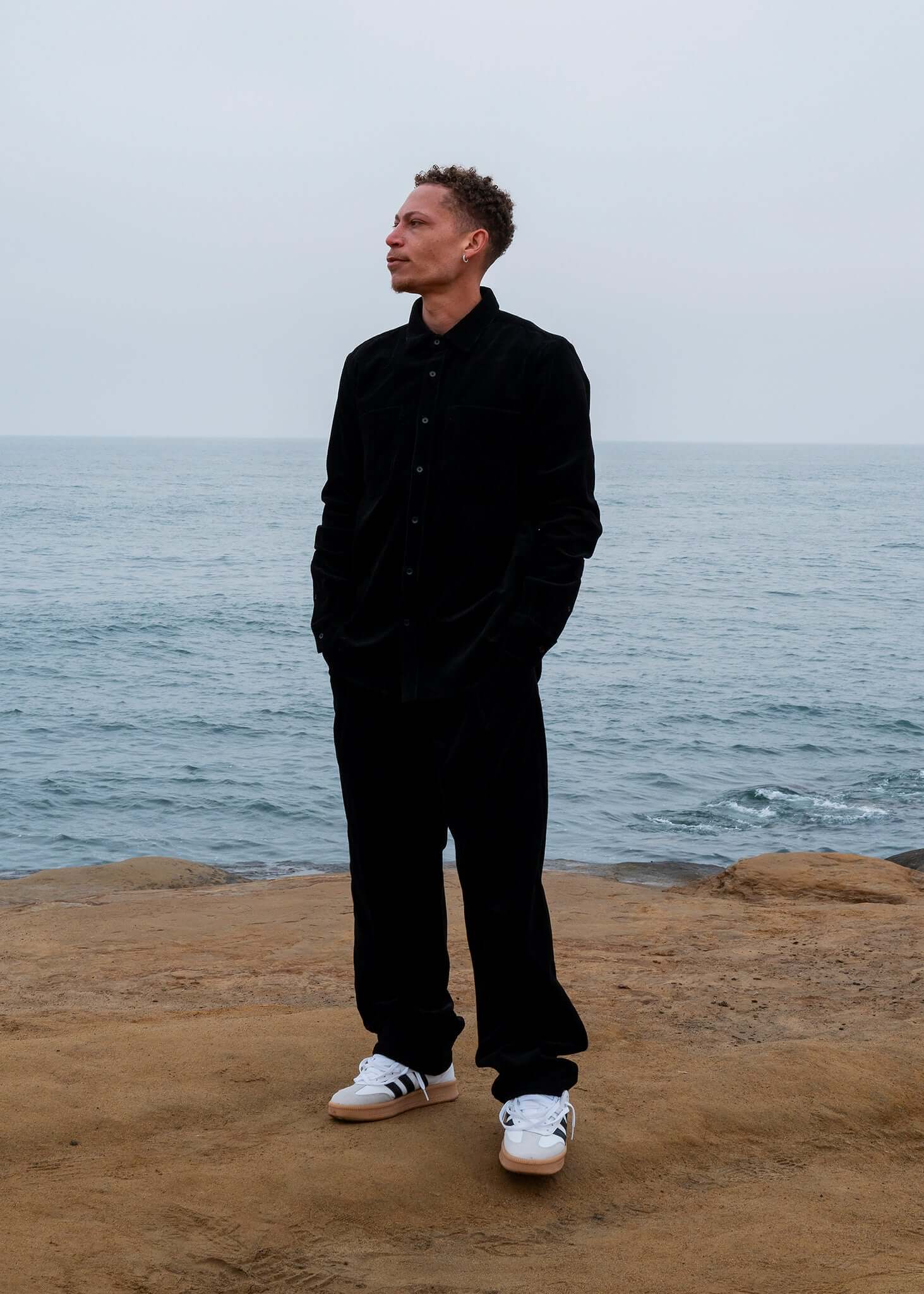 Man wearing Pleated Corduroy Trousers and a matching shirt by the sea, showcasing a relaxed and stylish look.