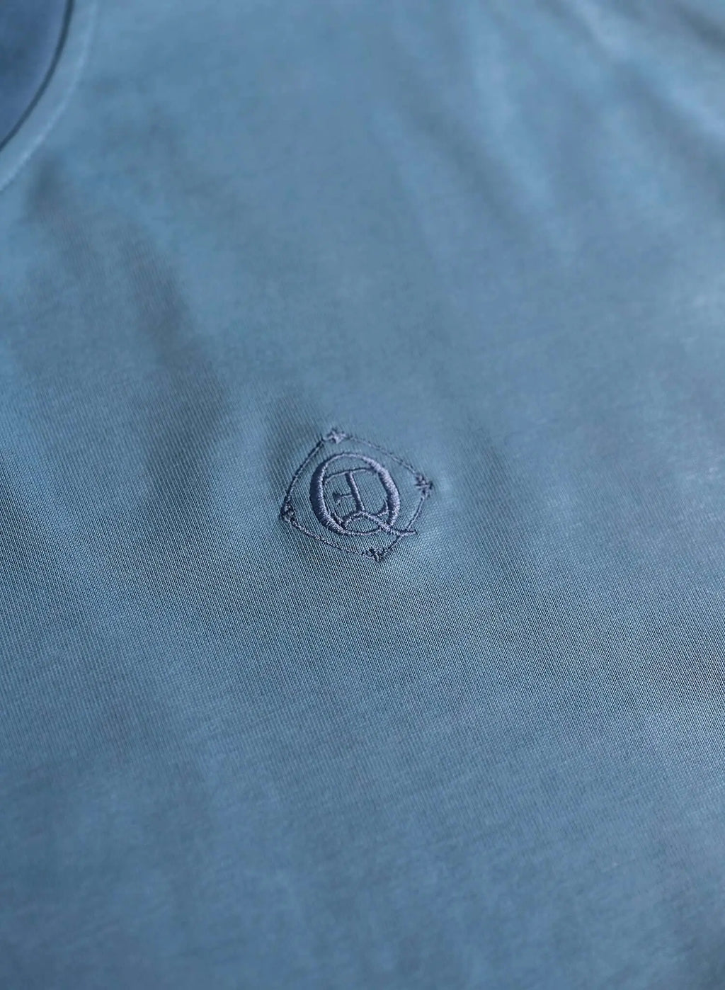Monogram embroidered cotton t-shirt close-up showing embroidered monogram logo on blue fabric.