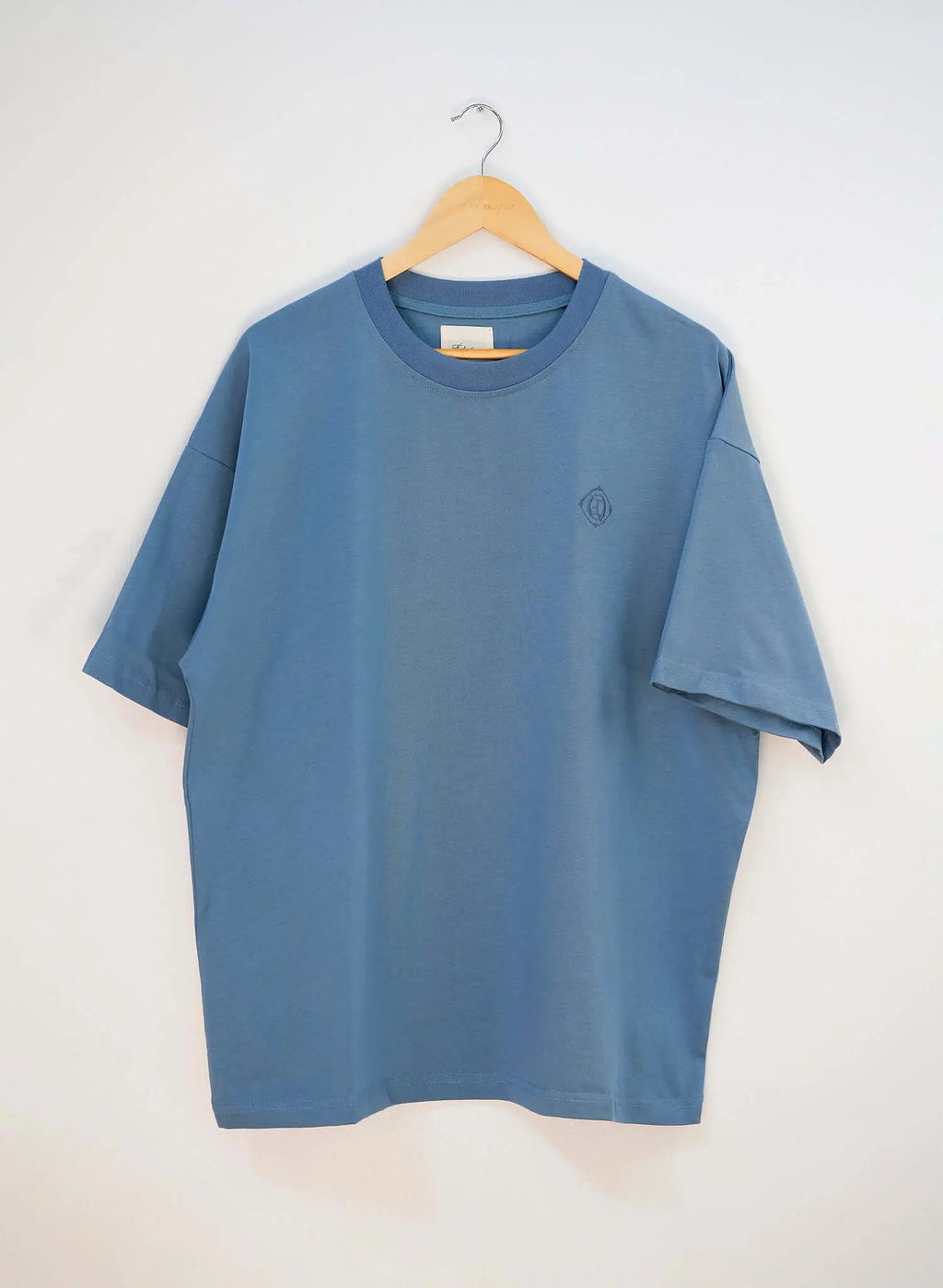 Monogram embroidered cotton t-shirt in blue hanging on a wooden hanger showcasing its clean silhouette.