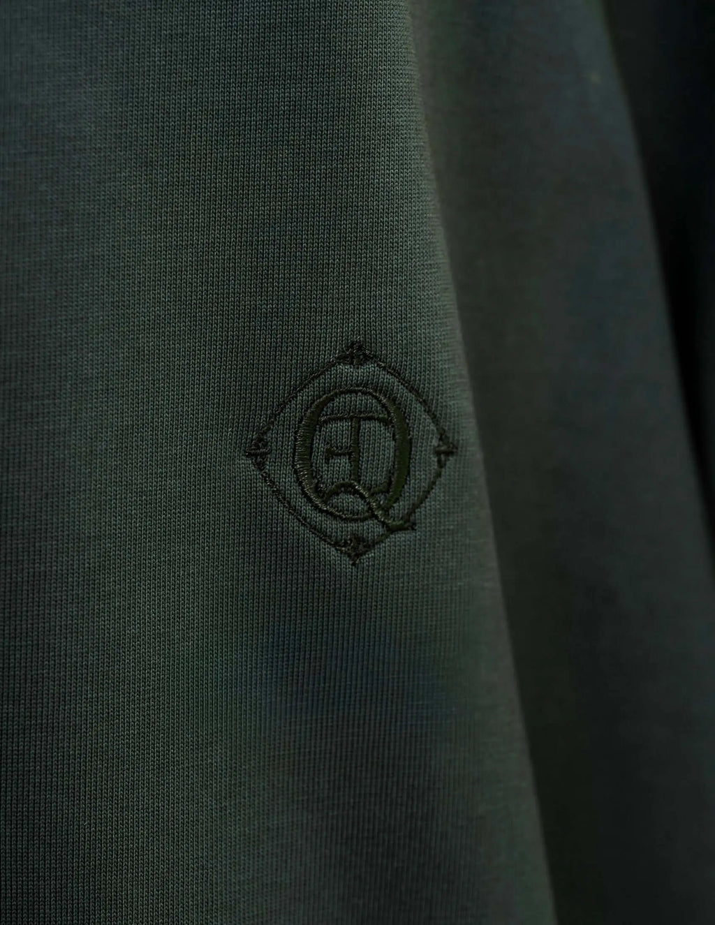 Close-up of embroidered monogram logo on monogram embroidered cotton t-shirt in emerald green.
