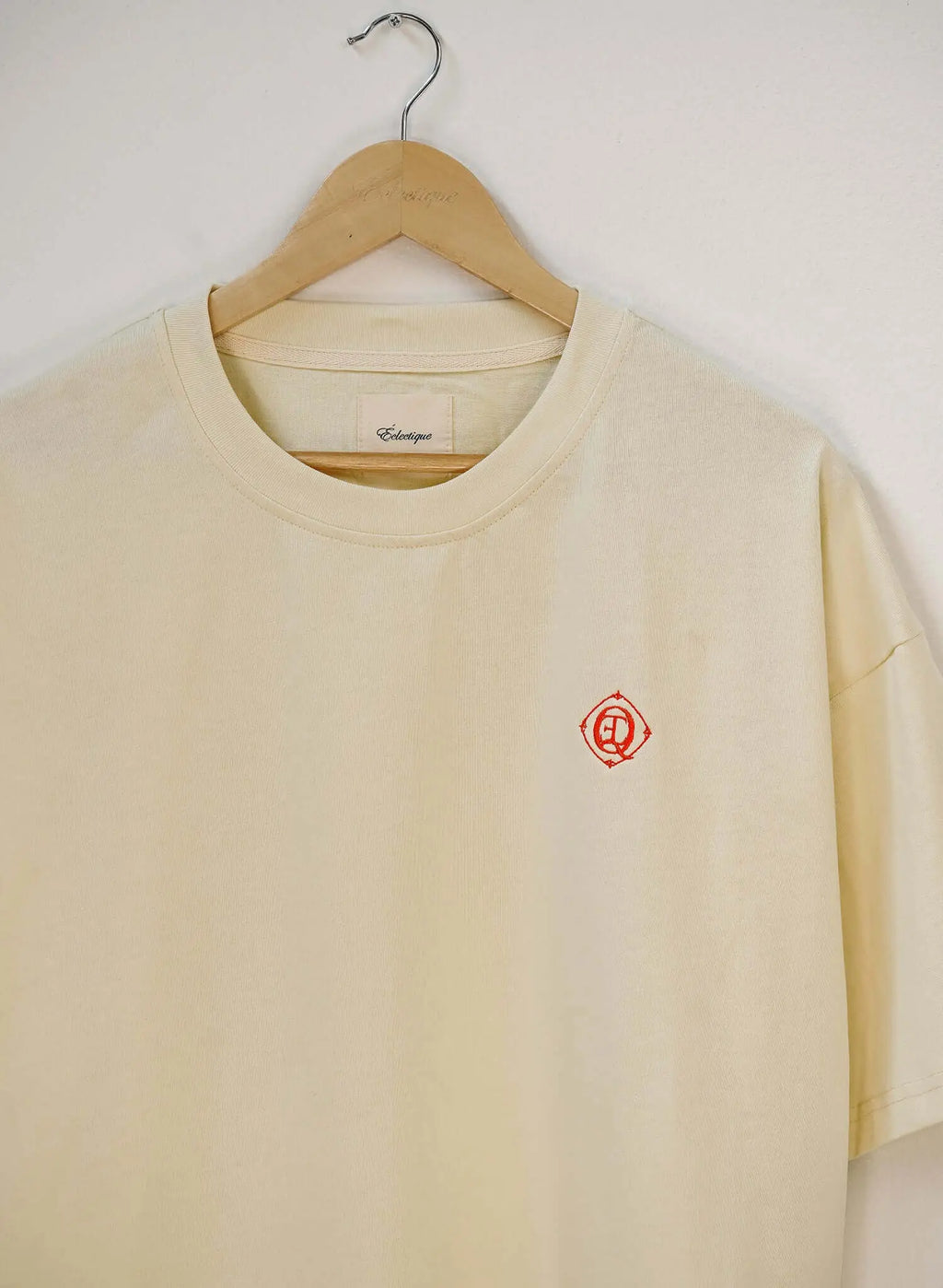Monogram embroidered cotton t-shirt in French vanilla hanging on a wooden hanger, featuring an embroidered logo.