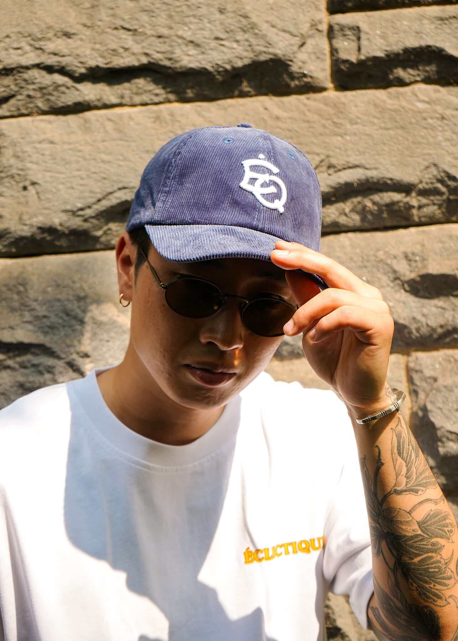 Man wearing a vintage corduroy dad hat and sunglasses, posing against a stone wall.