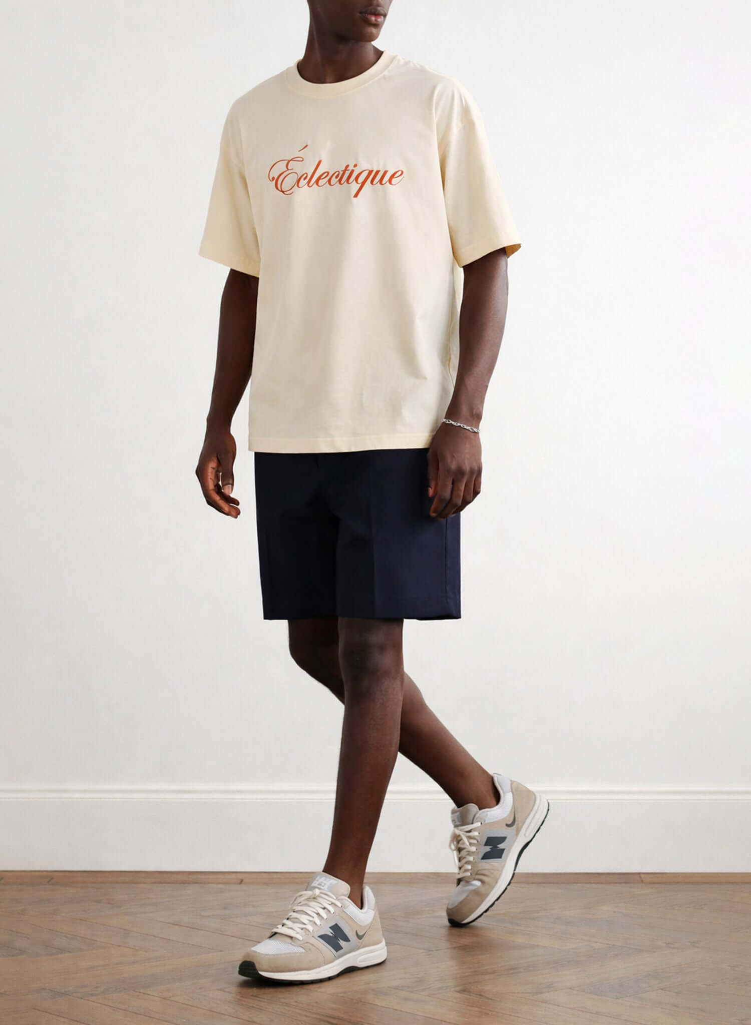 Model wearing Éclectique script logo embroidered cotton t-shirt in French vanilla with navy shorts and sneakers.