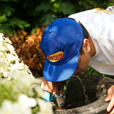 Person wearing a royal blue Seinfeld Vintage Logo Hat while leaning over a water fountain.
