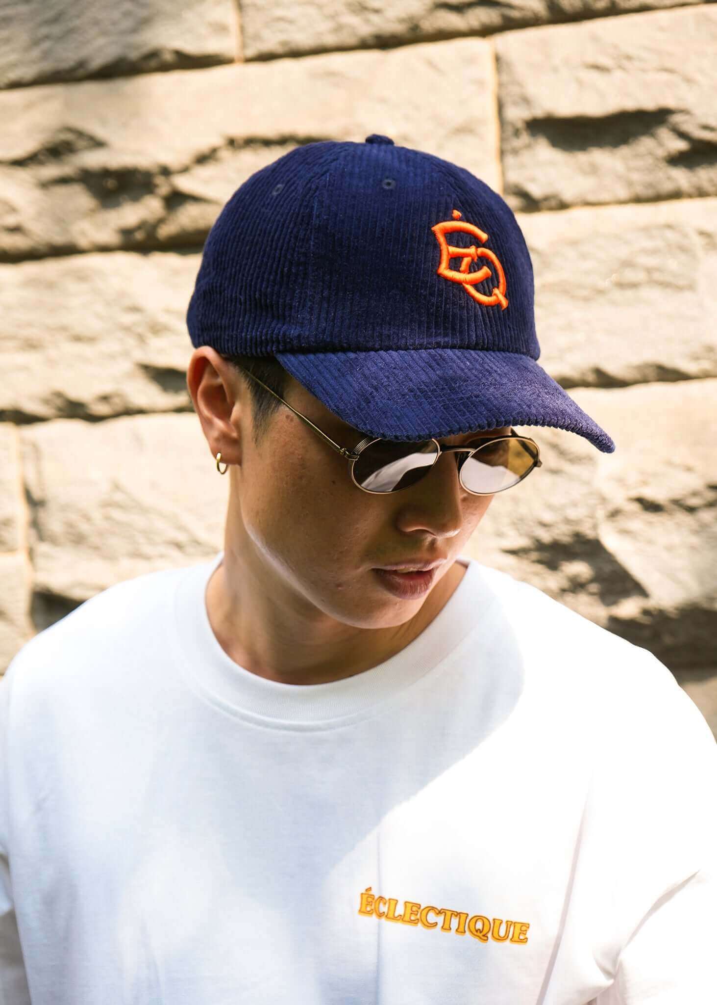 A model wearing a vintage corduroy dad hat and sunglasses, showcasing casual style against a stone wall.